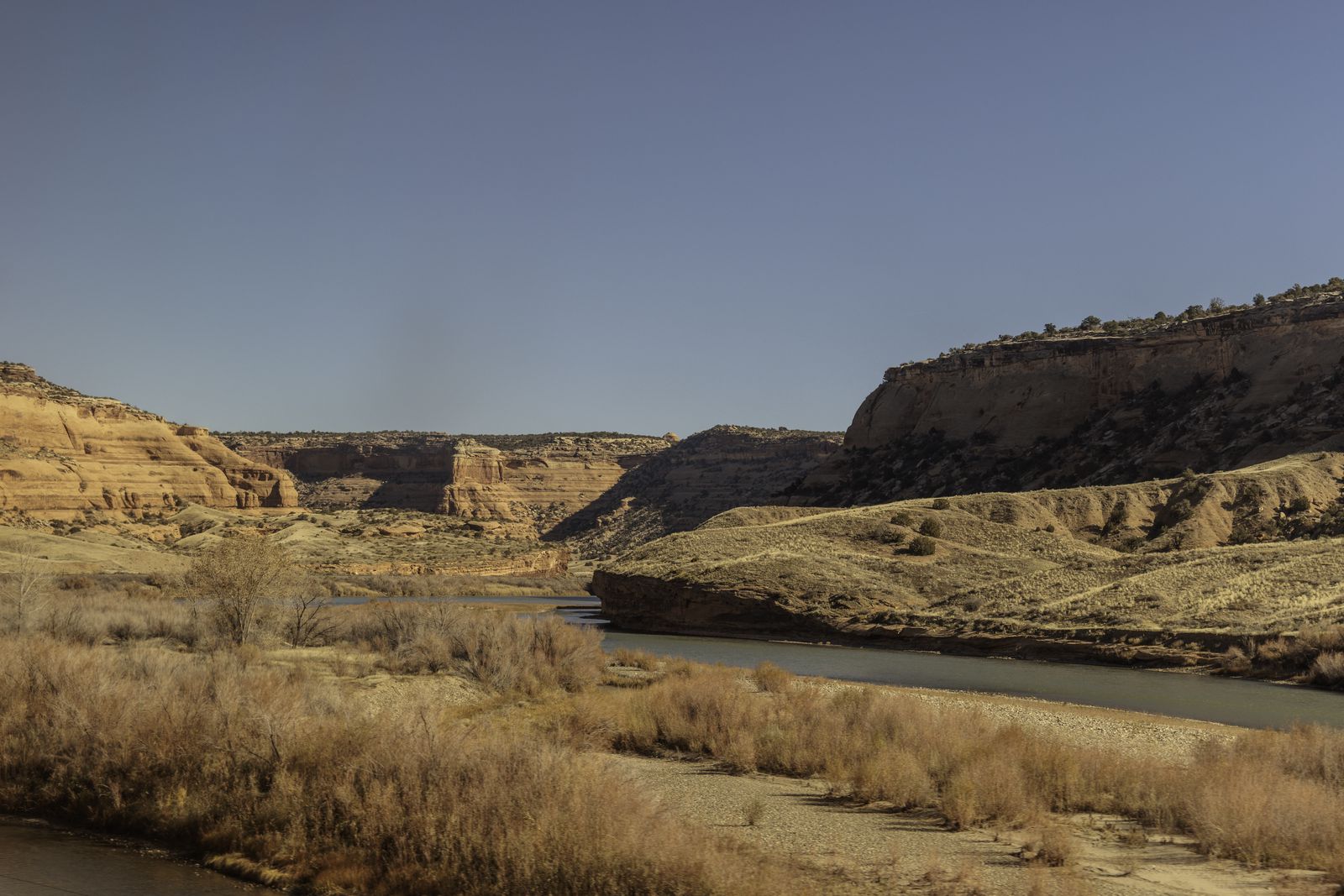 A desert canyon landscape with a winding river cutting through layered sedimentary rock formations somewhere in Eastern Utah.
